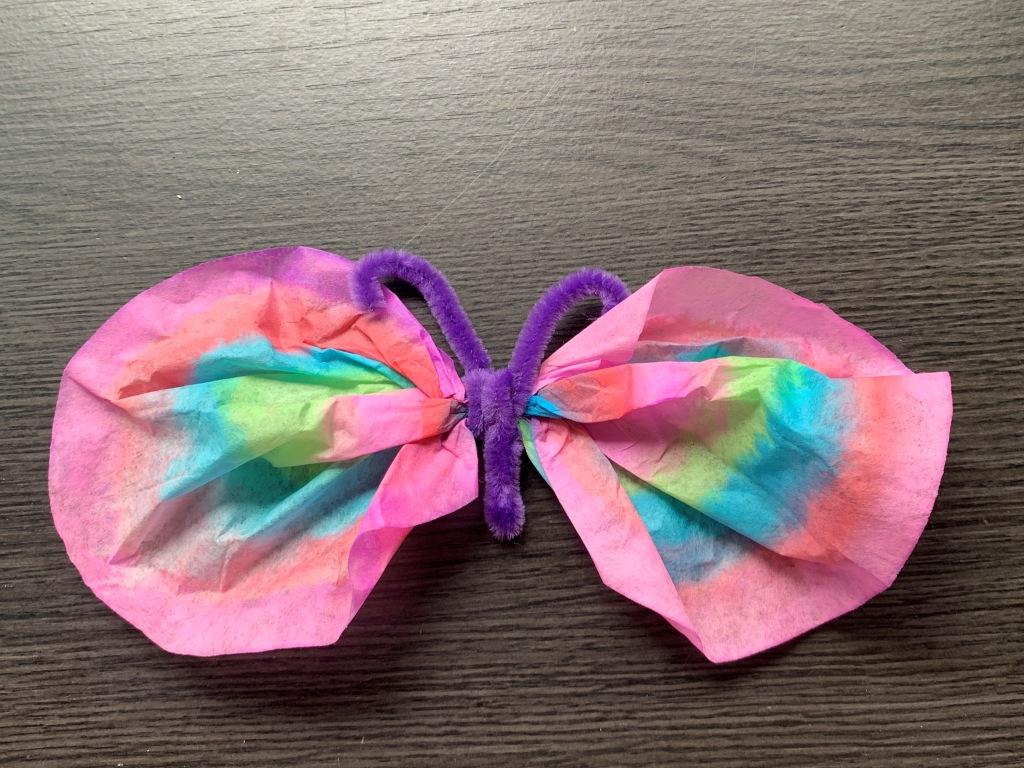 Shown is a finished craft using colored tissue paper and a pipe cleaner to create a butterfly.